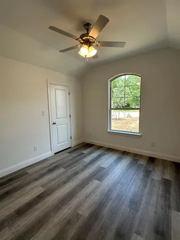 an empty room with wooden floor chandelier fan and windows