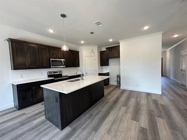 a large kitchen with stainless steel appliances granite countertop a stove top oven a sink dishwasher and a microwave with wooden floor