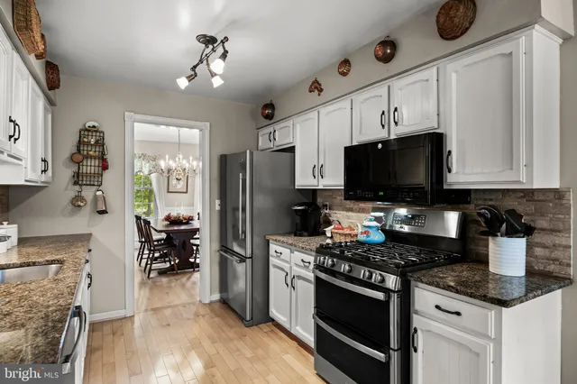 a kitchen with stainless steel appliances kitchen island granite countertop a stove top oven a sink dishwasher a dining table and chairs with wooden floor