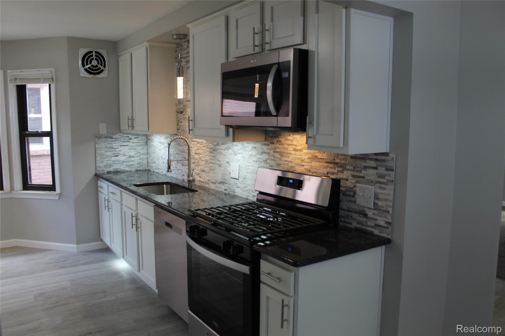 5543 Balfour Road Detroit, MI 48224 - Photo 9 of 54 Kitchen featuring light grey cabinetry, dark stone countertops, a mosaic tile backsplash, stainless steel appliances, and wood-finish flooring
