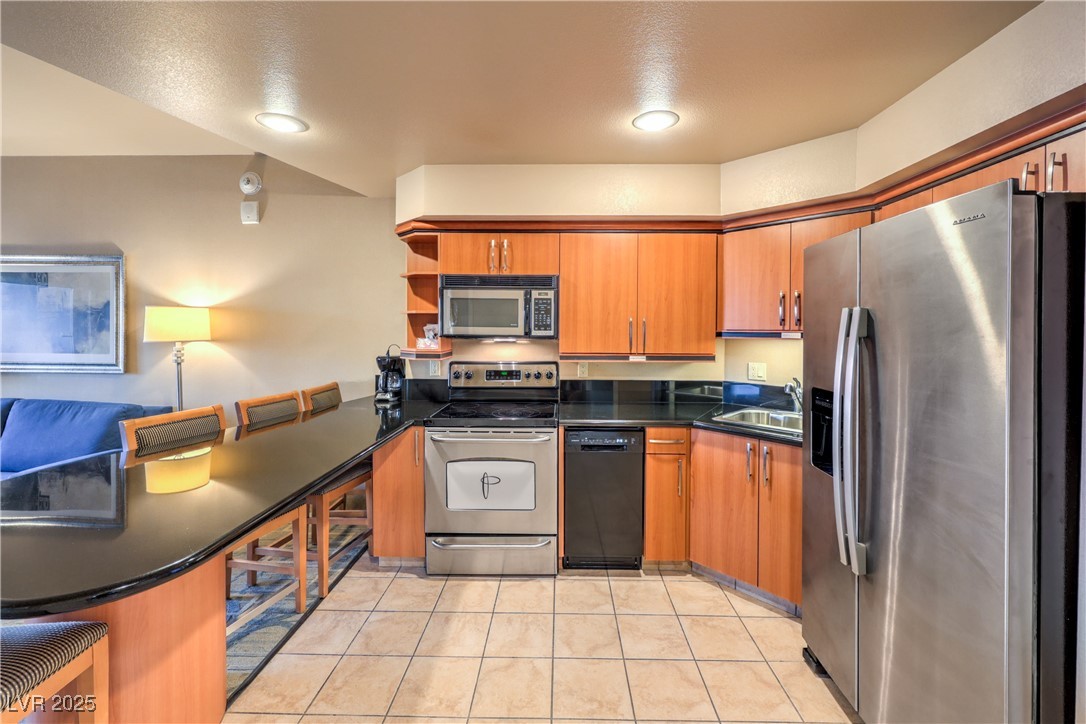 211 East Flamingo Road, Unit 1505 Las Vegas, NV 89169 - Photo 7 of 45 Kitchen featuring stainless steel appliances, brown cabinets, open shelves, light tile patterned flooring, and dark stone counters