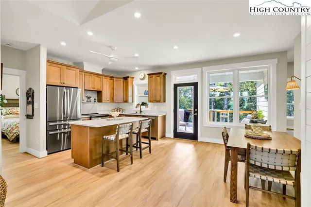 a kitchen with stainless steel appliances granite countertop a stove a refrigerator a sink a dining table and chairs with wooden floor