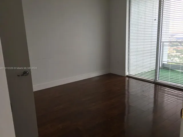 an empty room with wooden floor and windows with curtains