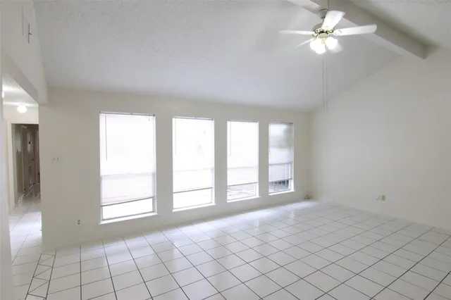 a view of an empty room with window and chandelier fan