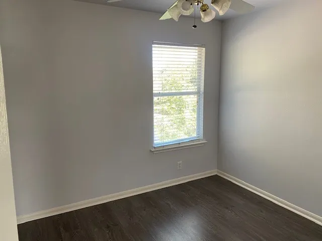 an empty room with wooden floor chandelier fan and windows