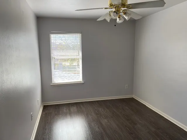 an empty room with wooden floor fan and windows