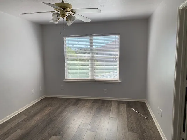 an empty room with wooden floor fan and windows