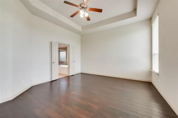 an empty room with wooden floor chandelier fan and windows