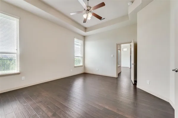 an empty room with wooden floor chandelier fan and windows