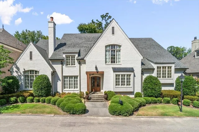 a view of a brick house with a yard plants and large tree