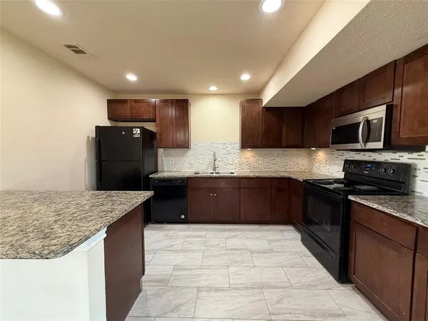 a large kitchen with stainless steel appliances granite countertop a refrigerator a stove a sink a microwave and wooden cabinets