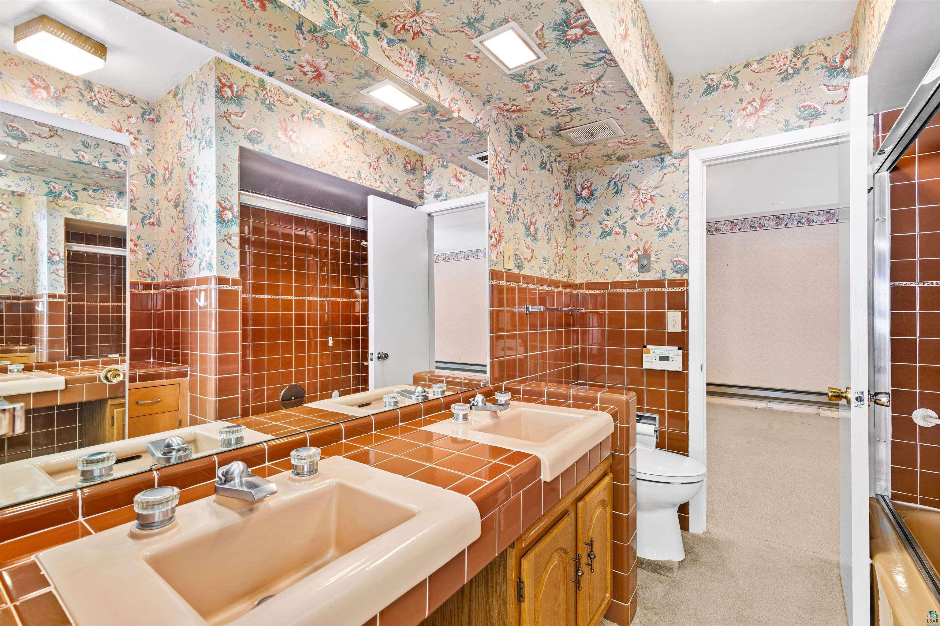 5781 South Pike Lake Road Duluth, MN 55811 - Photo 11 of 42 Bathroom featuring double vanity, tile walls, wallpapered walls, wainscoting, and enclosed tub / shower combo