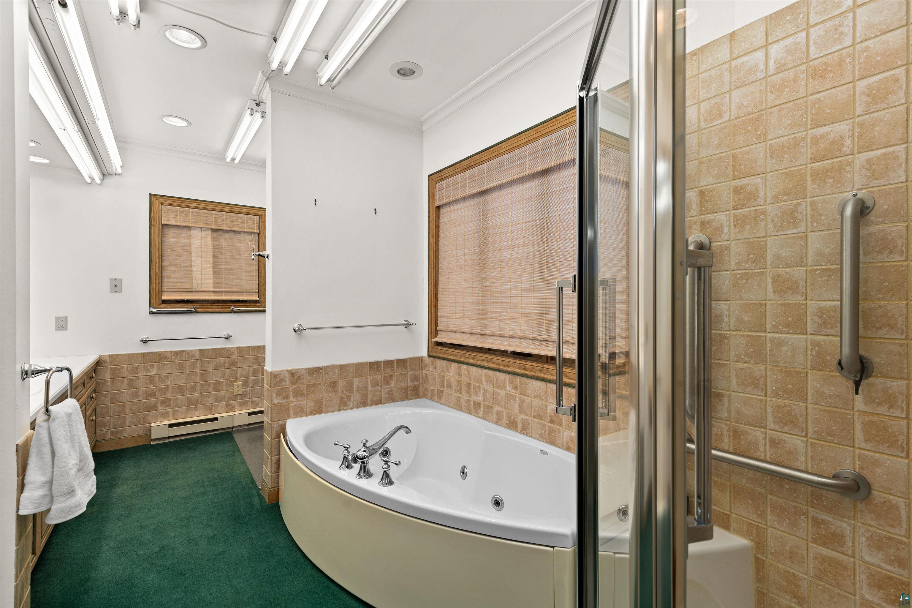 5781 South Pike Lake Road Duluth, MN 55811 - Photo 17 of 42 Bathroom featuring a tub with jets, tile walls, wainscoting, a stall shower, and a baseboard radiator