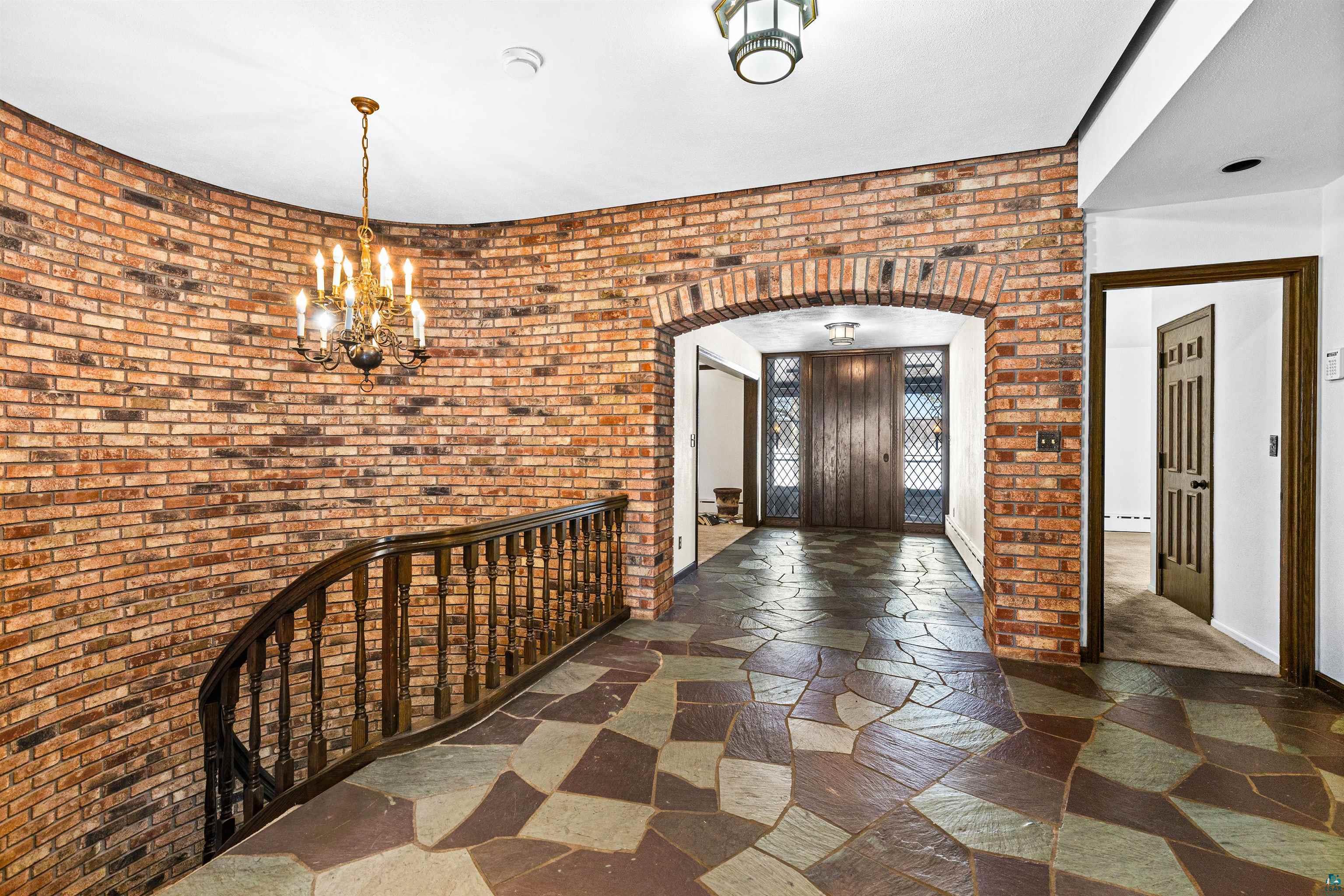 5781 South Pike Lake Road Duluth, MN 55811 - Photo 28 of 42 Foyer with brick wall, arched walkways, a chandelier, and dark stone finish flooring
