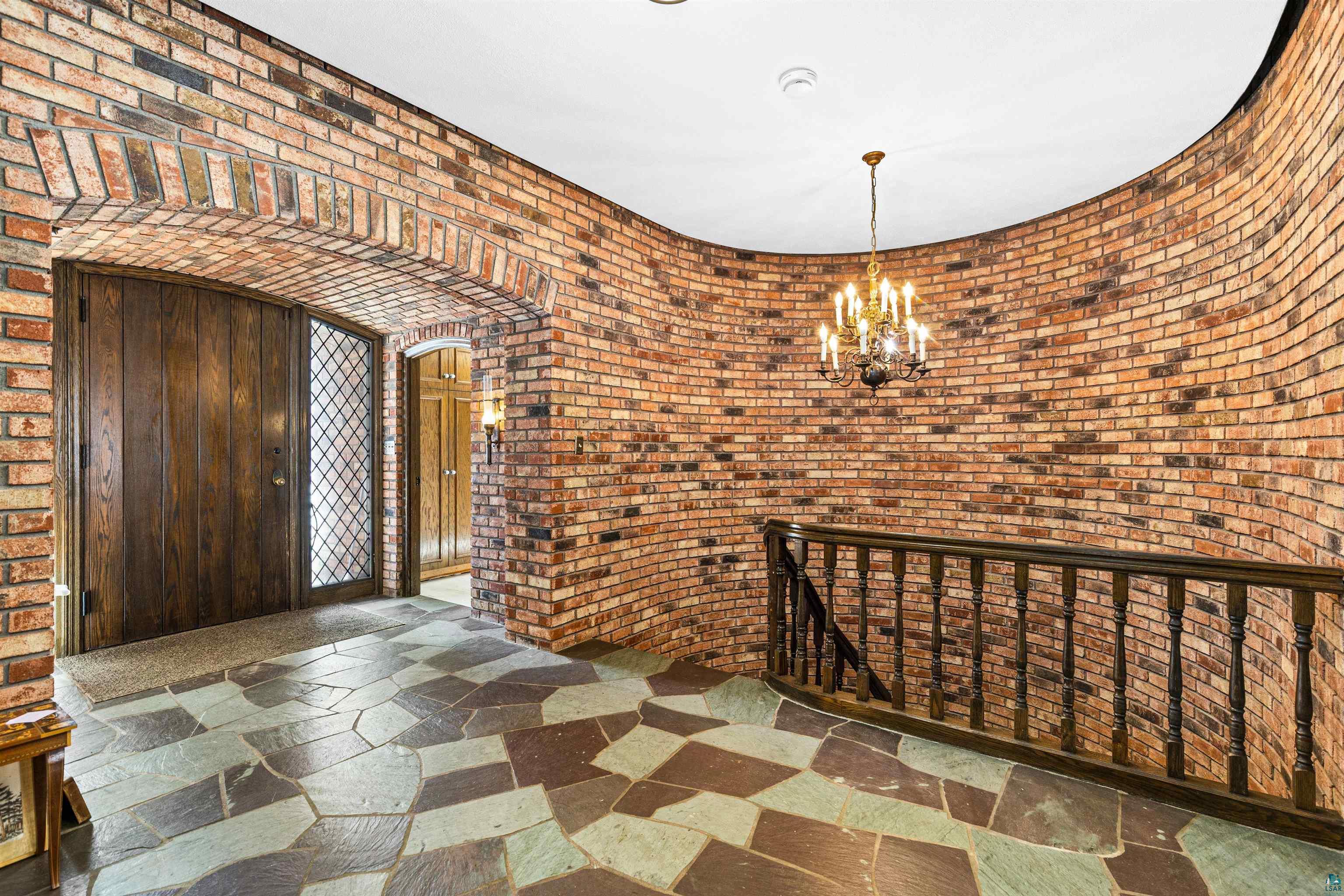 5781 South Pike Lake Road Duluth, MN 55811 - Photo 29 of 42 Entryway with arched walkways, stone tile flooring, a chandelier, and brick wall