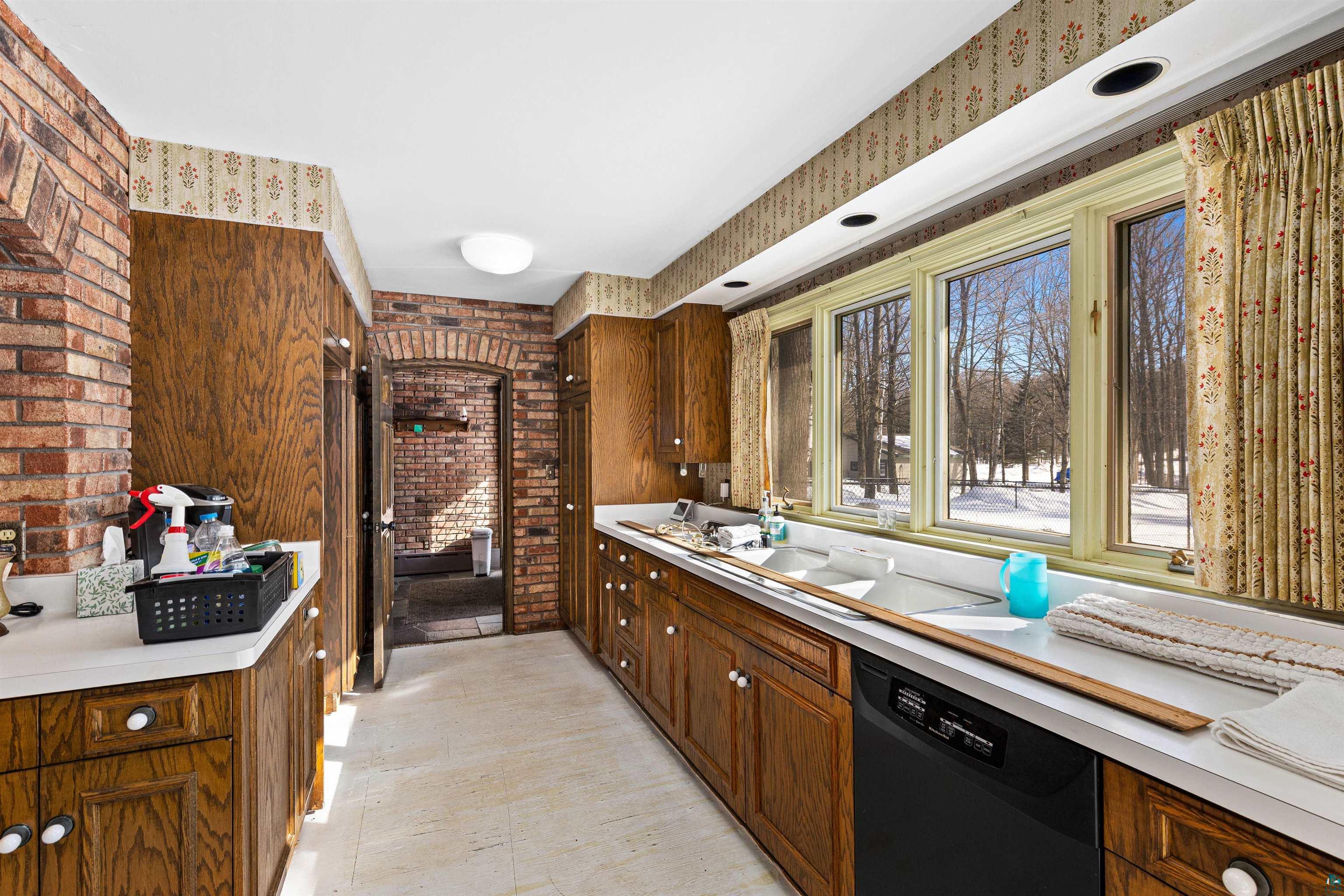 5781 South Pike Lake Road Duluth, MN 55811 - Photo 32 of 42 Kitchen featuring light countertops, black dishwasher, brick wall, and wood finish cabinetry