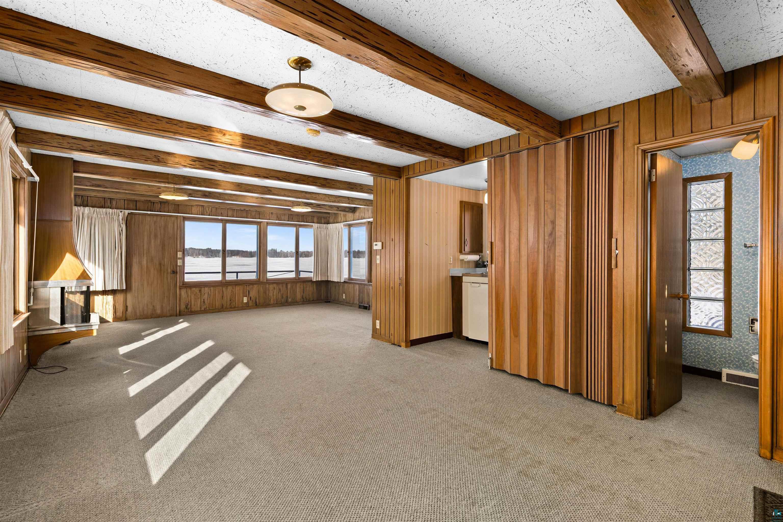 5781 South Pike Lake Road Duluth, MN 55811 - Photo 40 of 42 Unfurnished living room featuring light colored carpet, wood walls, beamed ceiling, and a textured ceiling