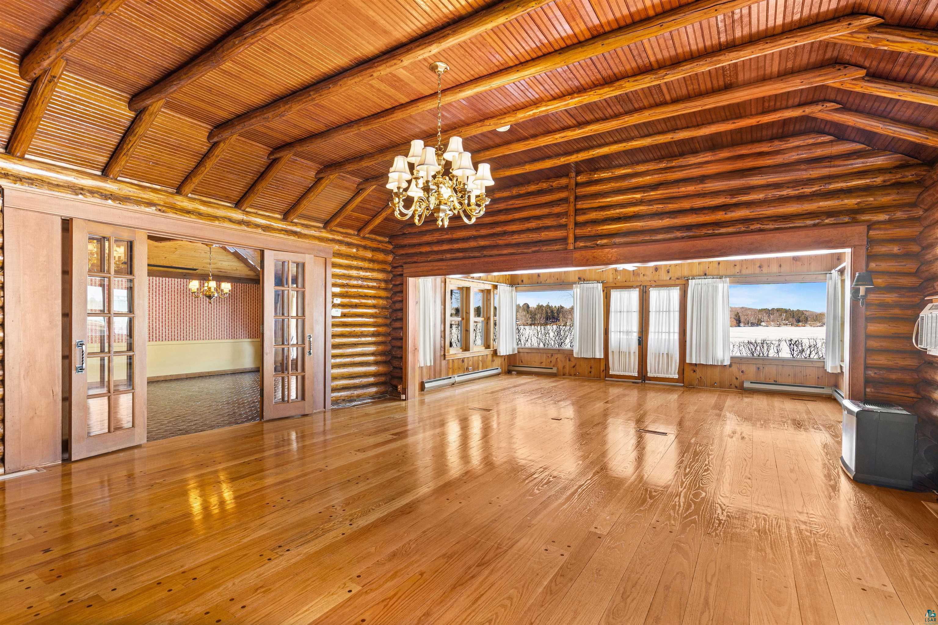5781 South Pike Lake Road Duluth, MN 55811 - Photo 8 of 42 Unfurnished living room featuring french doors, suspended lighting, log walls, hardwood / wood-style floors, and a wainscoted wall