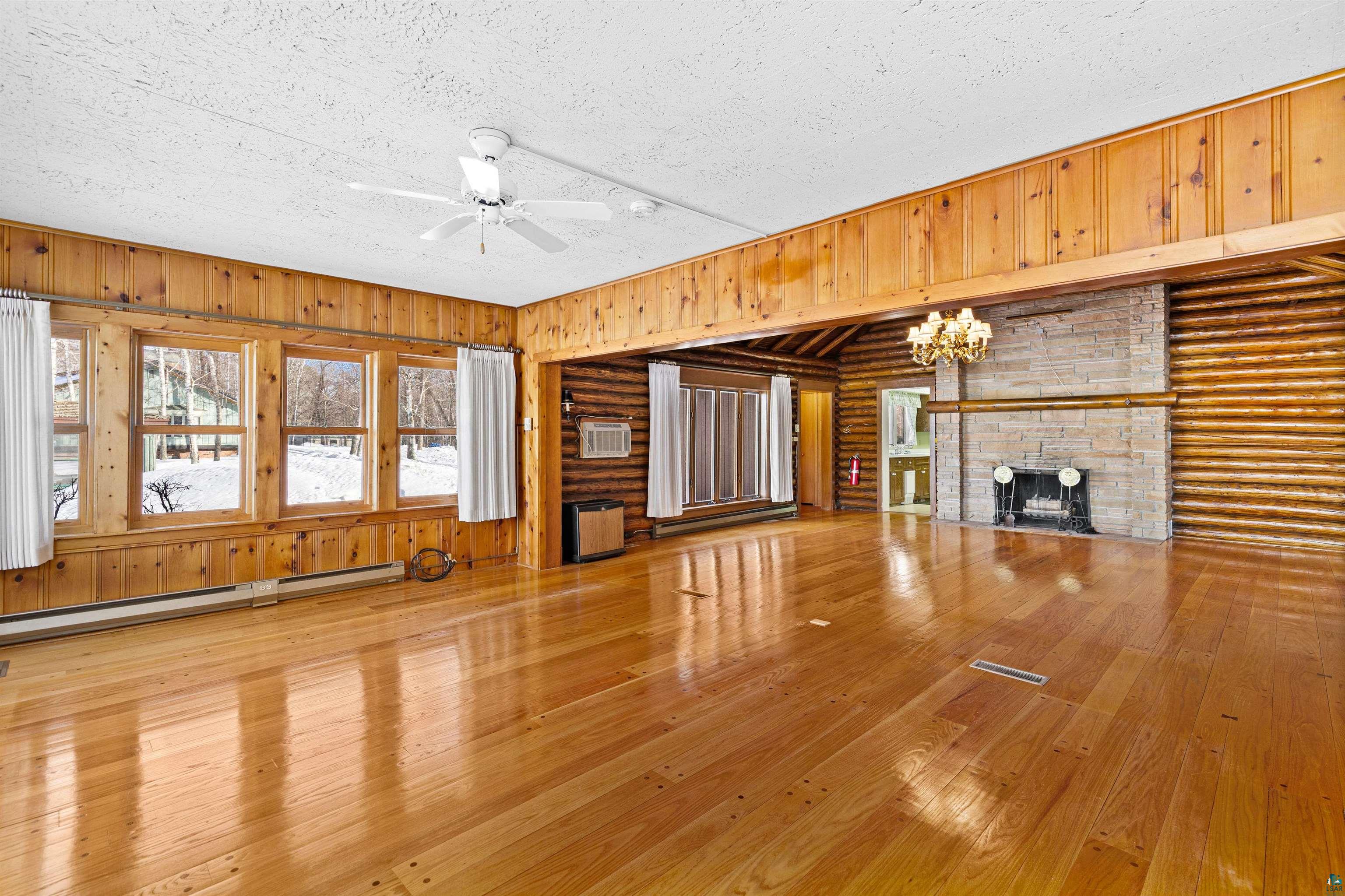 5781 South Pike Lake Road Duluth, MN 55811 - Photo 9 of 42 Unfurnished living room featuring a stone fireplace, a ceiling fan, hardwood / wood-style flooring, baseboard heating, and hanging lights