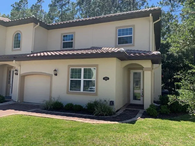 a view of a house with a yard plants and large tree