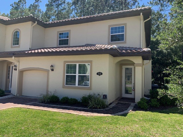 a view of a house with a yard plants and large tree