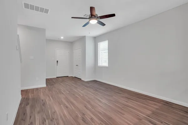 an empty room with wooden floor ceiling fan and windows