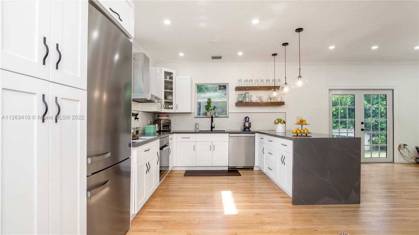 635 Bird Road Coral Gables, FL 33146 - Photo 15 of 35 a large kitchen with stainless steel appliances kitchen island a large counter top and a wooden floors