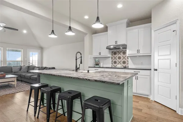 a kitchen with stainless steel appliances granite countertop a sink a stove a refrigerator and island with wooden floor