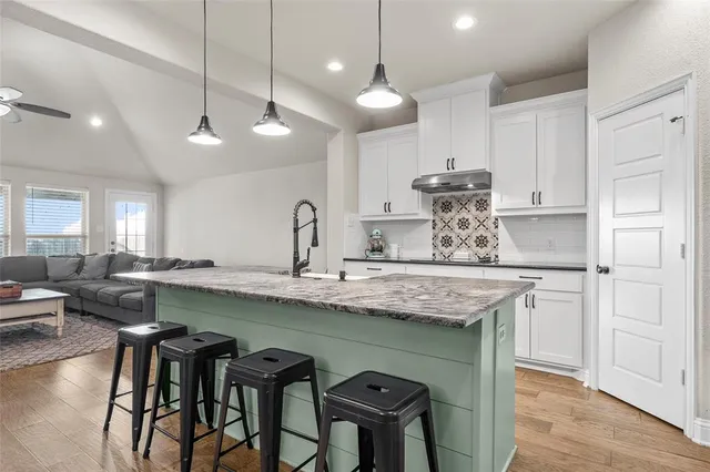 a kitchen with stainless steel appliances granite countertop a sink a stove a refrigerator and island with wooden floor