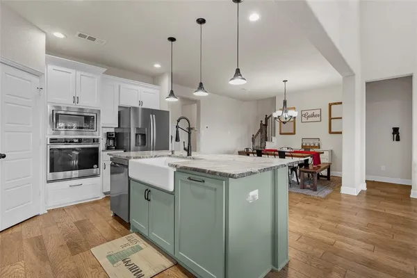 a kitchen with kitchen island a stove a sink a microwave oven a refrigerator and white cabinets with wooden floor