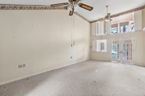 an empty room with a chandelier fan and windows
