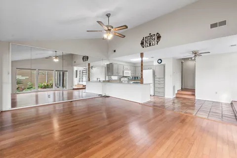 a view of an empty room and kitchen view with wooden floor
