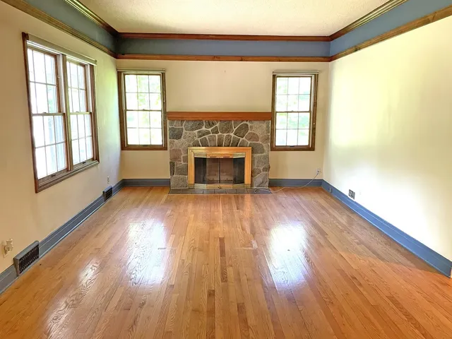an empty room with wooden floor fireplace and windows