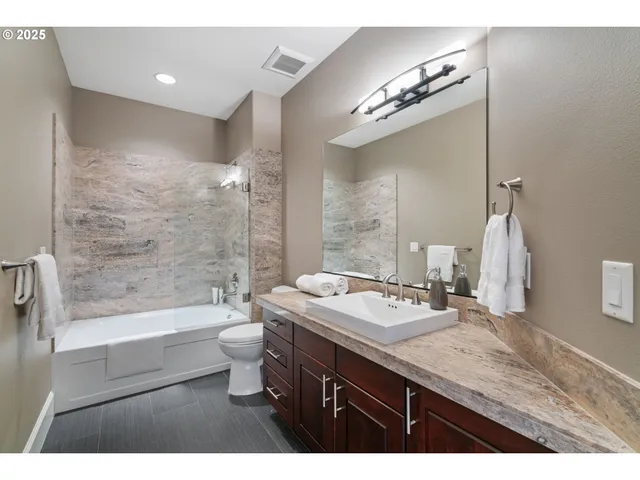 a bathroom with a granite countertop sink a toilet a large mirror and shower