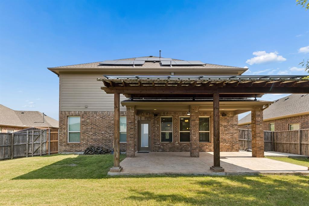 537 Hunt Farms Road Fate, TX 75189 - Photo 35 of 36 Expansive backyard featuring a covered patio with a wooden pergola, a brick and siding exterior, multiple windows, and rooftop solar panels
