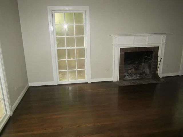 an empty room with wooden floor fire place and windows