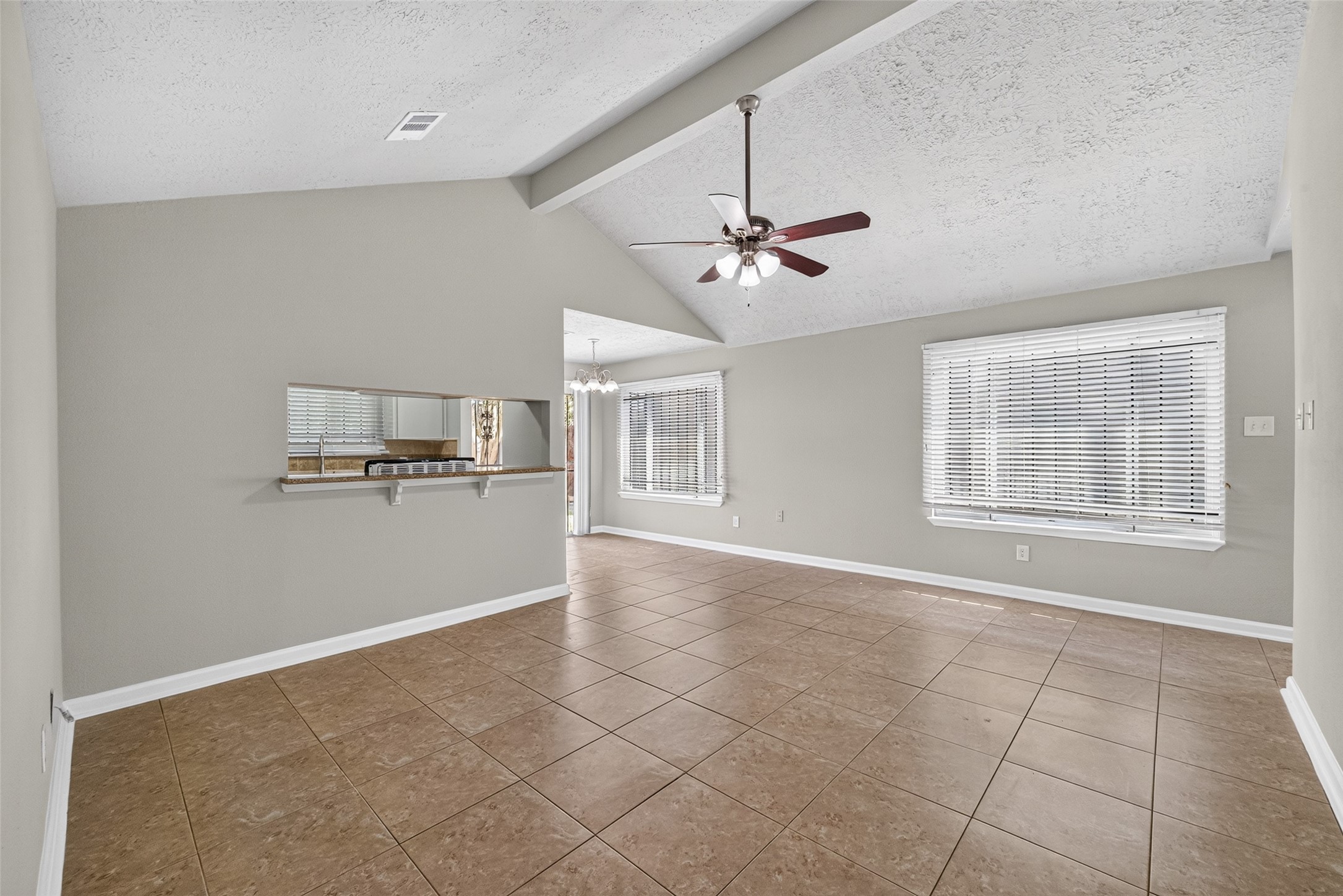 16203 Beck Ridge Drive Houston, TX 77053 - Photo 7 of 29 Living area with vaulted ceiling, elegant tile flooring, and abundant natural light from large windows, complemented by a ceiling fan and a stylish pass-through to the dining space.