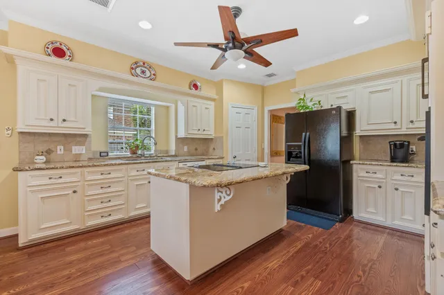 a kitchen with stainless steel appliances granite countertop a refrigerator a stove a sink and white cabinets with wooden floor