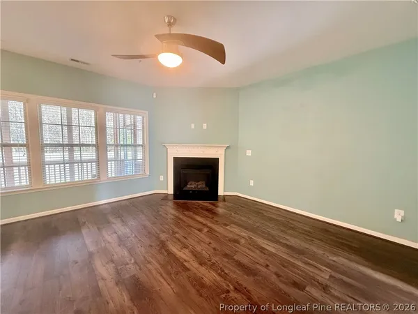 an empty room with wooden floor fireplace and windows