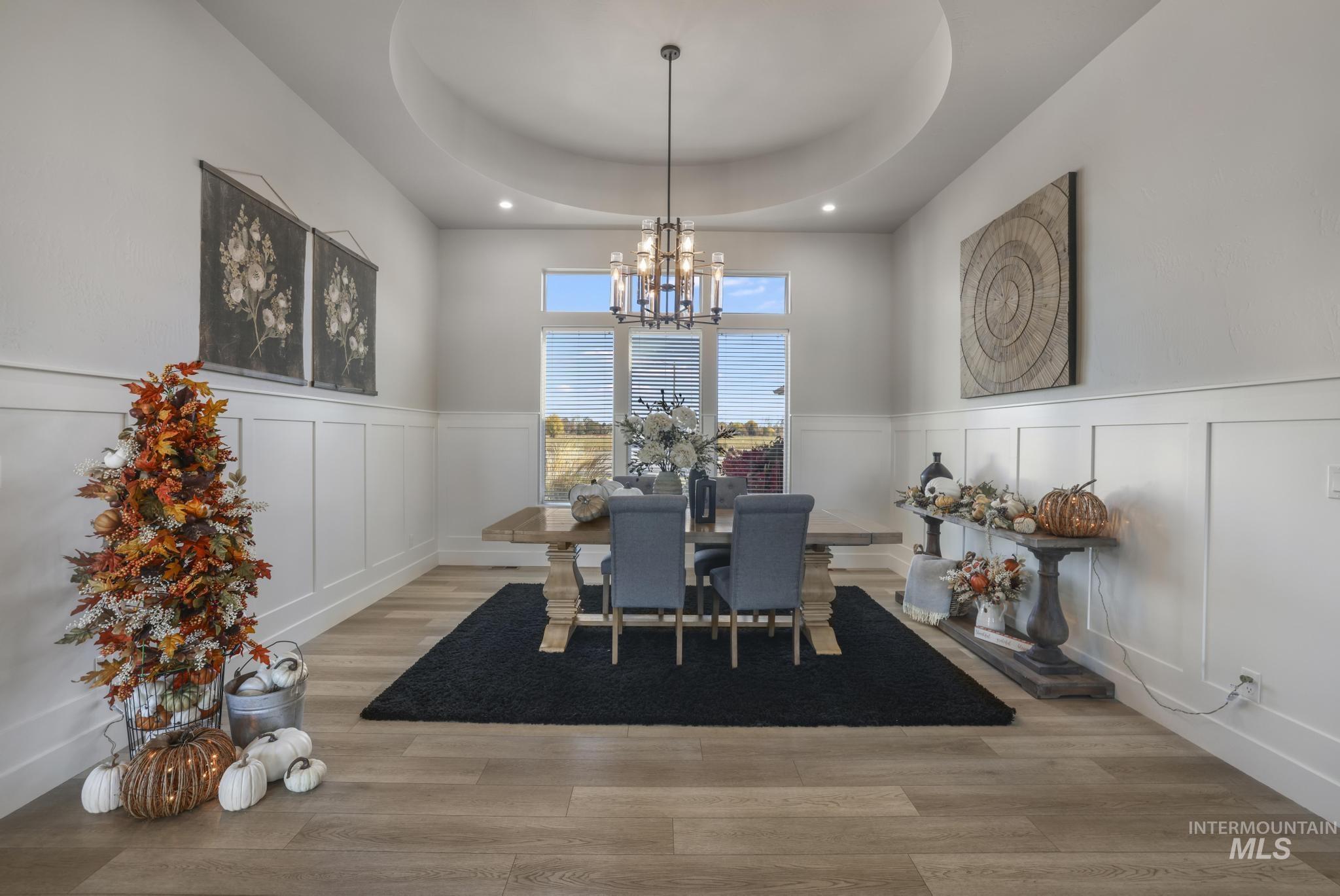 439 Meadowview Lane Twin Falls, ID 83301 - Photo 4 of 48 Dining space with a decorative wall, light wood-style flooring, a wainscoted wall, a chandelier, and a raised ceiling