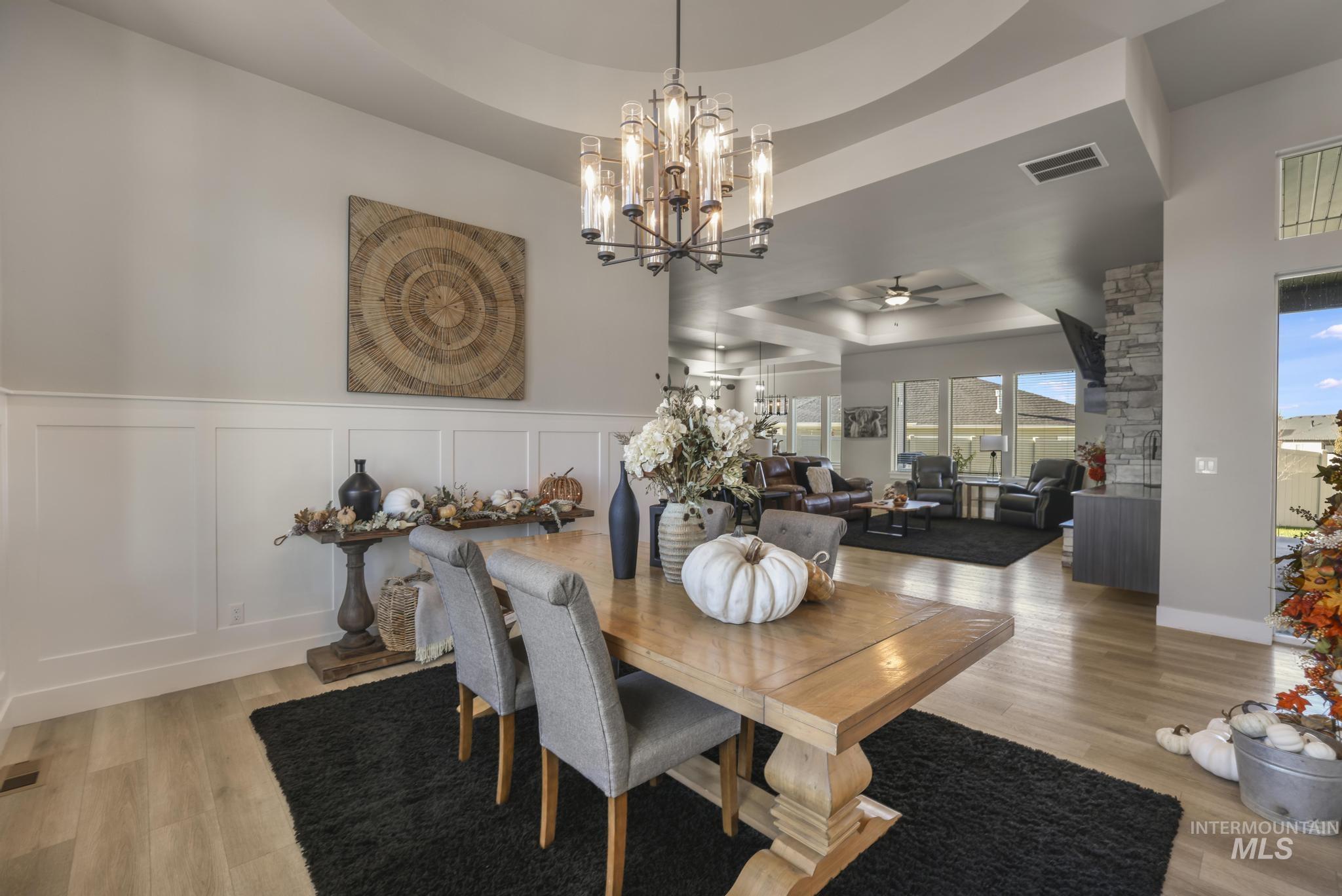 439 Meadowview Lane Twin Falls, ID 83301 - Photo 5 of 48 Dining space with a raised ceiling, a ceiling fan, light wood-type flooring, a chandelier, and a decorative wall