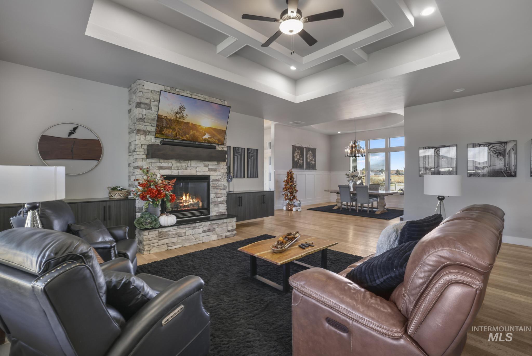 439 Meadowview Lane Twin Falls, ID 83301 - Photo 9 of 48 Living area featuring a stone fireplace, coffered ceiling, wainscoting, wood finished floors, and a ceiling fan