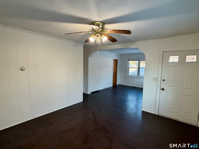 a view of an empty room with wooden floor and a ceiling fan