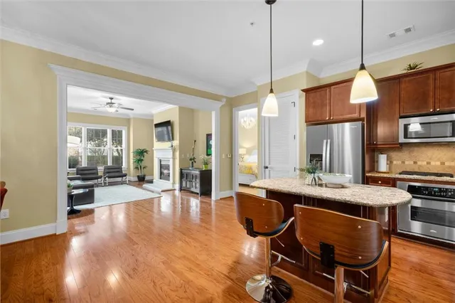 a kitchen with stainless steel appliances granite countertop a stove top oven a refrigerator a dining table and chairs with wooden floor