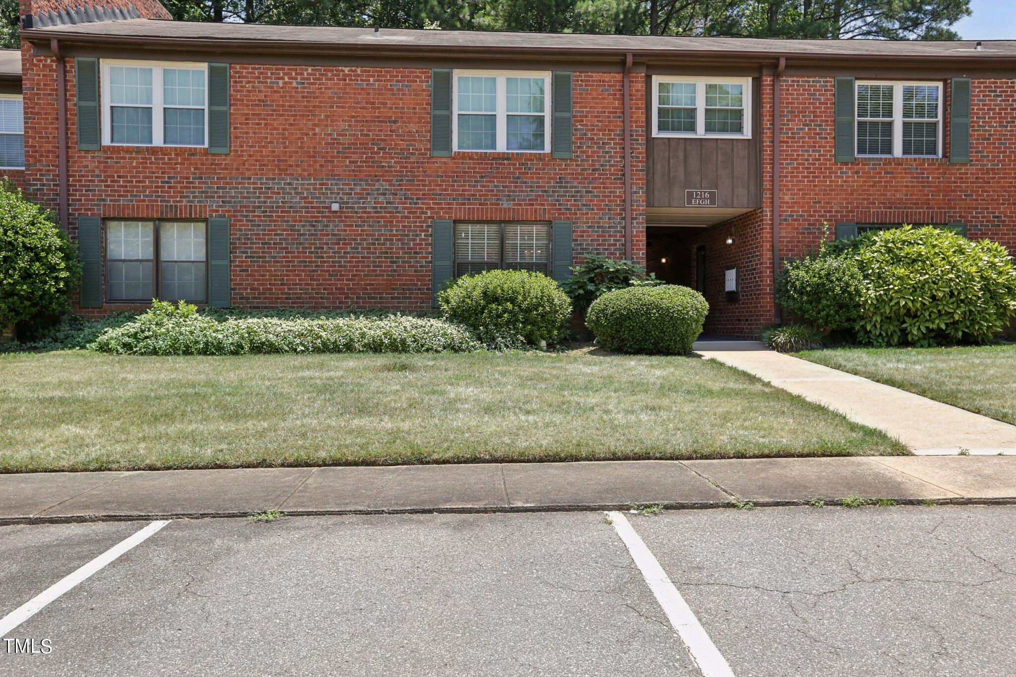 1216 Manassas Court, Unit E Raleigh, NC 27609 - Photo 2 of 20 a view of a brick house with a yard plants and large tree