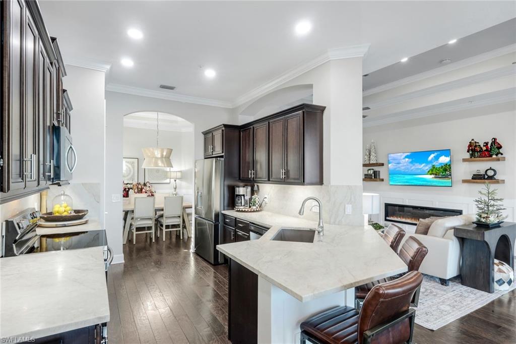 8783 Coastline Court, Unit 202 Naples, FL 34120 - Photo 14 of 49 a kitchen with stainless steel appliances kitchen island granite countertop a stove a refrigerator a dining table and chairs with wooden floor