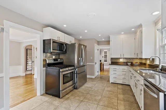 a view of an empty room and kitchen with wooden floor