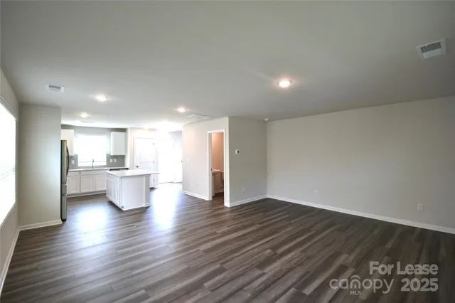 a view of an empty room and kitchen with wooden floor