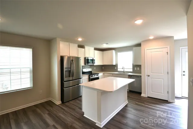a large kitchen with a center island wooden floor stainless steel appliances and windows