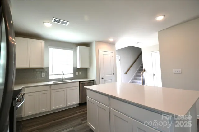 a kitchen with a sink dishwasher and white cabinets with wooden floor